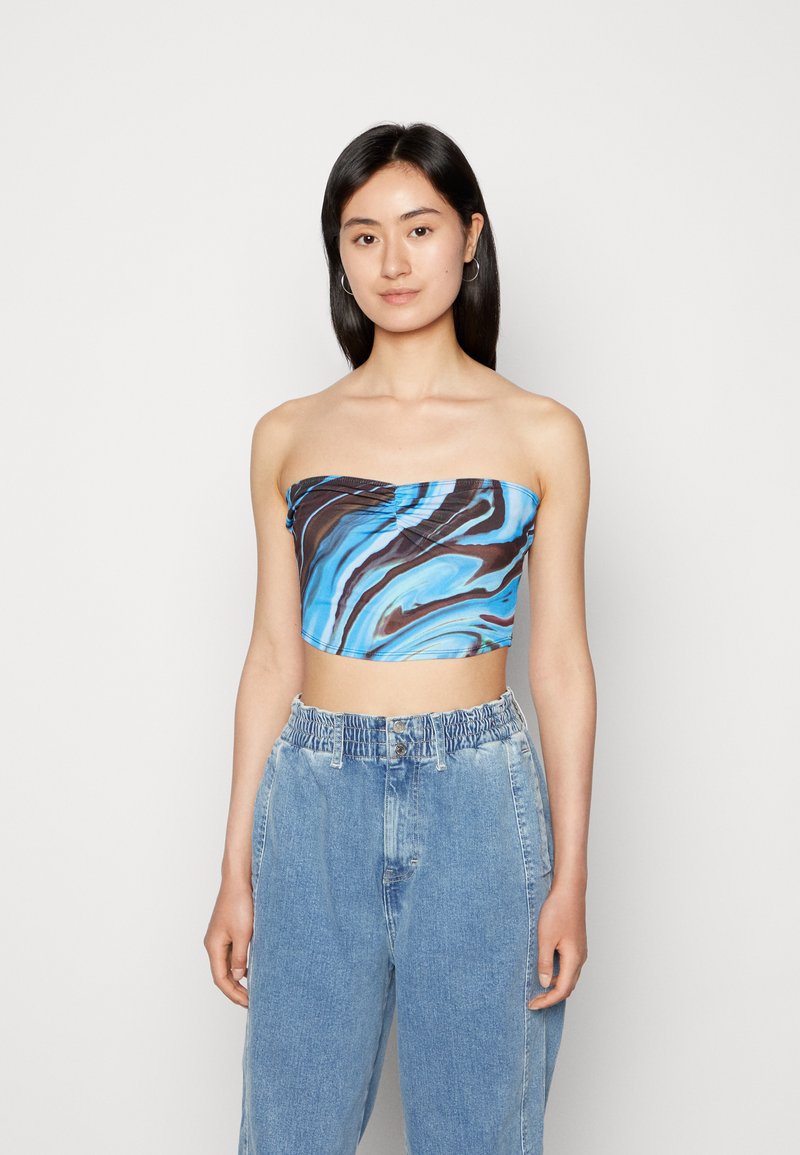 Top cropped sem alças em padrão espiral azul e castanho, com um design frontal torcido. Combinado com calças de ganga de cintura alta, em azul claro.