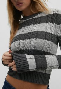 Pull en tricot rayé gris et gris clair avec des motifs en relief, des manches et un ourlet côtelés. Design court et ajusté avec un tissu texturé.