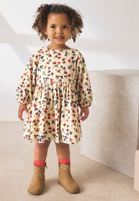 Floral-patterned beige dress with puff sleeves and gathered waist, paired with brown ankle boots and pink socks. Smooth, soft fabric.