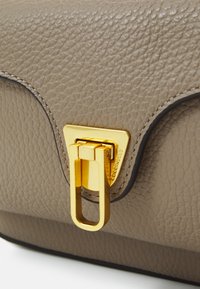 Graue, strukturierte Lederhandtasche mit einem goldenen Metallverschluss in dreieckigem Design. Die Kanten haben einen kontrastierenden dunklen Rand.