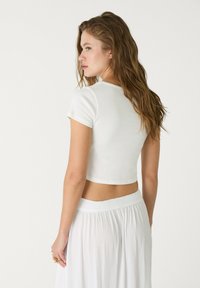 Afskåret hvid t-shirt lavet af blødt stof, med rund hals og korte ærmer, parret med en svævende hvid nederdel med smocket talje.