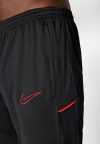 Sorte atletiske shorts lavet af glat stof. Har et rødt Nike-logo og en rød accentlinje på lommen. Elastisk talje for bedre pasform.
