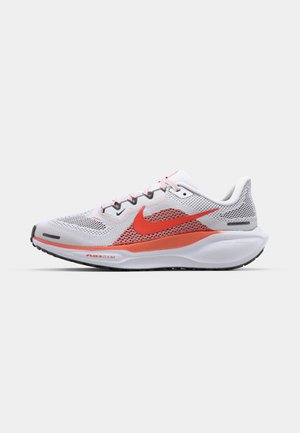 Zapatillas blancas con una parte superior de malla transpirable, que cuentan con un prominente swoosh rojo, acentos rojos y una suela blanca acolchada.