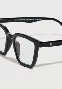 Μαύρα ορθογώνια γυαλιά με διάφανα φακούς, με χοντρά πλαστικά πλαίσια και διακριτική σήμανση στο βραχίονα. Ομαλή υφή επιφάνειας.