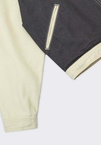 Camicia a maniche lunghe multicolore con una parte superiore nera e una parte inferiore crema, con cuciture a contrasto e una fessura laterale.