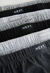 Fünf Paare elastischer Unterwäsche in Schwarz, Grau und Hellgrau, mit beschrifteten Bündchen, auf denen "NEXT" in weißer Schrift steht.