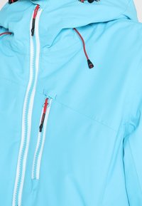 Veste d'extérieur bleu clair avec fermetures éclair blanches, tirettes rouges et cordons réglables à capuche.