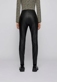 Svarta fusk läder skinny byxor med en mjuk textur och slim fit. Detaljerad sömnad längs sömmarna. Bärs med en mönstrad långärmad topp.