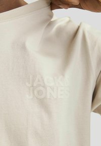 Beige puuvillane t-särk ümmarguse kaelusega, millel on sarnases värvitoonis tekstureeritud logo "JACK & JONES" rinna piirkonnas. Sile tekstuur.