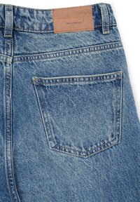 Poche arrière de jeans en denim bleu avec une étiquette en cuir brun portant la mention "Collection Denim" cousue au-dessus.