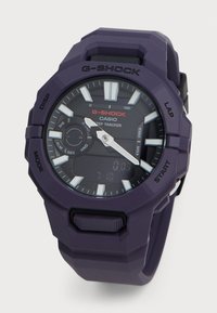 Montre G-SHOCK violette avec un boîtier en résine texturée, affichage analogique et numérique, accents blancs, fonction chronomètre et bracelet robuste.