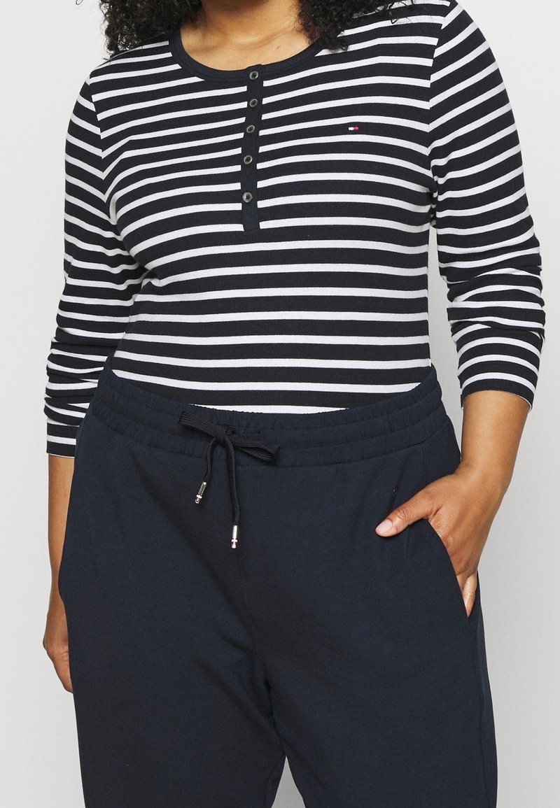 Lange mouw, marineblauw en wit gestreept shirt met knoopdetails. Gecombineerd met marineblauwe sweatpants met een elastische tailleband en zijzakken.