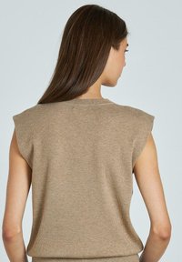 Top de punto sin mangas en color beige, confeccionado en un material suave; presenta un escote redondo y relleno en los hombros para dar estructura. Textura suave, diseño minimalista.