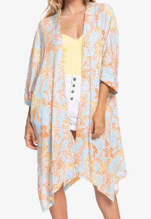 Kimono floral ample avec des fleurs orange et jaune sur fond bleu clair, porté sur un haut jaune et un short blanc à boutons.