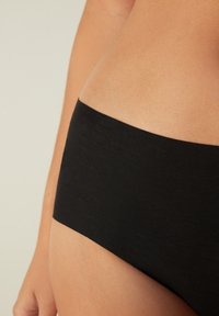 Černé bavlněné hipster kalhotky, s hladkým povrchem a elastickým pasem, zobrazené na pozadí s světlou pletí.