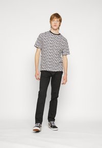Camiseta gráfica en blanco y negro con el logo de Levi's repetido, combinada con jeans negros y zapatillas negras con un diseño estampado.
