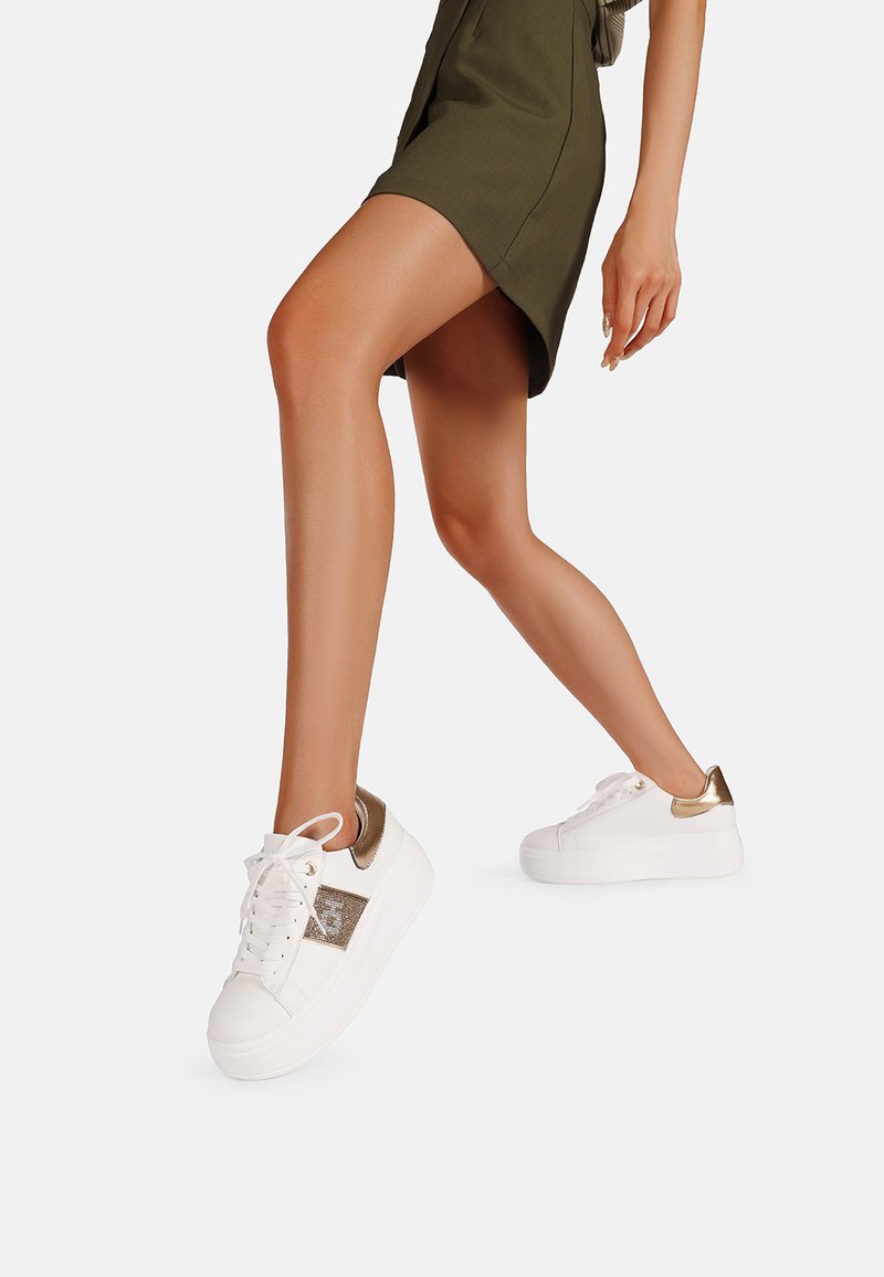 Sneaker bianca con dettagli dorati, pannello laterale texturizzato, punta rotonda e suola piatta. Design con lacci, finitura liscia e collo imbottito.