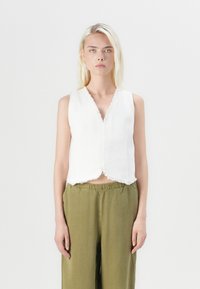 Witte mouwloze top met een V-hals, ruwe randen en een cropped ontwerp, gecombineerd met olijfgroene losse broek.