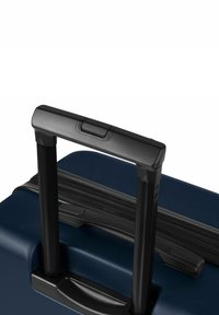 Valise rigide bleue avec une poignée noire rétractable et des fermetures éclair. Surface texturée, forme rectangulaire et deux boutons supérieurs pour le réglage de la poignée.