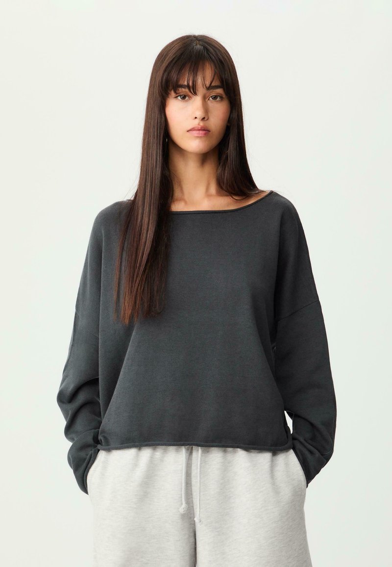 Dunkelgraues, übergroßes Sweatshirt mit weitem Ausschnitt und langen Ärmeln, kombiniert mit grauen Jogginghosen. Glatte Textur, lockere Passform.