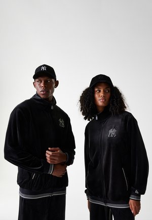 Black velour jackets with zip front, white accent stripes at cuffs and hem, and embroidered logo. Black caps complement the outfits.