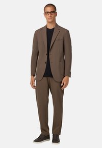 Ruskea pikkutakki, jossa on yhteensopivat housut, valmistettu sileästä kankaasta. Pikkutakissa on viisto kaulus, yksi rintatasku ja kaksi etutaskua.