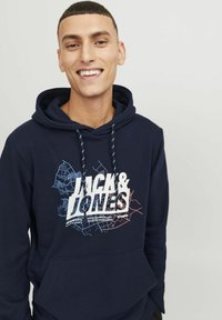 Sudadera azul marino con un estampado gráfico que presenta líneas blancas y de colores, capucha con cordones y bolsillo canguro en la parte delantera. Textura de tela suave.