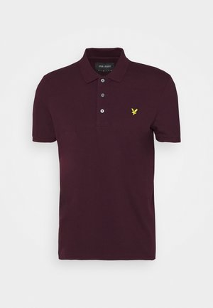 Fioletowa polo z krótkim rękawem, z trzema guzikami i małym żółtym logo orła na lewej piersi.