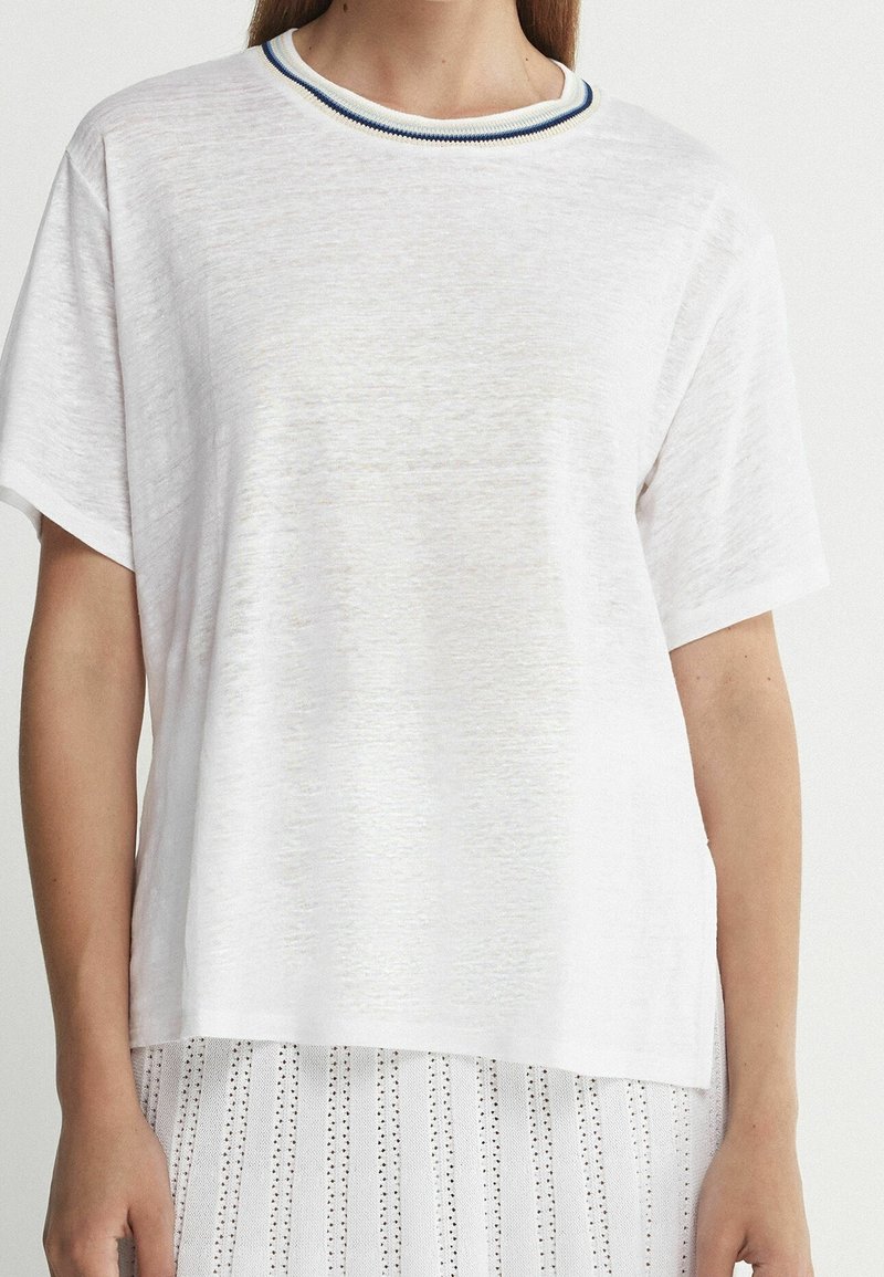 Femme portant un t-shirt blanc à manches courtes avec un col rayé bleu et beige et une jupe blanche à motifs.
