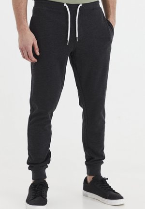 Gray sweatpants with a tapered fit, elastic waistband, white drawstrings, and side pockets, paired with black sneakers.