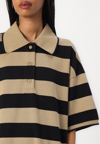 Beige och svart randig polo med krage, tre knappar och korta ärmar. Slät textur.