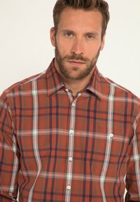 Koszula na guziki w kratę w odcieniach czerwieni, niebieskiego i bieli. Posiada usztywniany kołnierzyk oraz dwa guziki na przedniej kieszeni. Wykonana z bawełny.