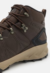 Bota de senderismo marrón con parte superior de cuero texturizado y malla, que cuenta con una suela resistente, talón reforzado y detalle del logo en el lateral.
