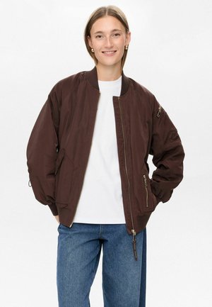 Brown bomber jacket with a zipper closure, ribbed cuffs, two side pockets, and embroidered text detail along the zipper. Worn over a white shirt.