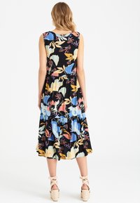 Robe midi florale en tissu noir, ornée de motifs floraux colorés, sans manches, avec une jupe à volants froncés et un col arrondi.