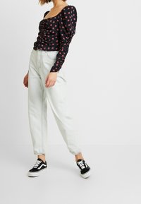 Top nero a maniche lunghe con scollatura quadrata, abbinato a jeans chiari dal fit rilassato e sneaker nere Vans.