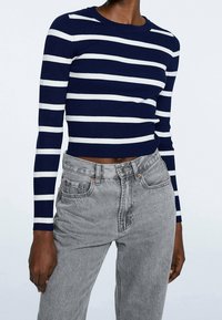 Maglione a righe navy e bianche, a costine, con maniche lunghe, abbinato a jeans grigi a vita alta con un classico design a cinque tasche.