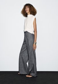 White sleeveless top paired with wide-leg gray trousers featuring a textured, faintly striped pattern. Sandals and a metallic cuff bracelet are included.