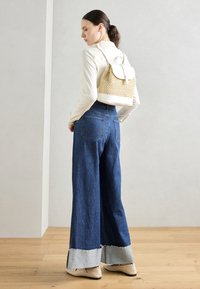 Ljust vävt ryggsäck med en strukturerad form, kombinerad med högmidjade denimjeans med vida ben som har en kontrasterande fåll.
