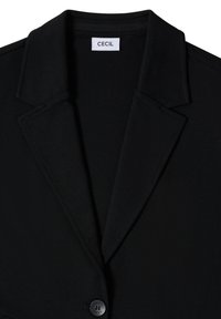 Blazer noir avec revers larges, un bouton visible et une étiquette blanche indiquant "CECIL" à l'intérieur du col.
