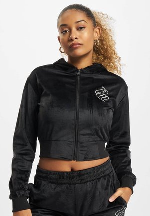 Schwarzer, kurzer Hoodie aus weichem, samtigem Material mit einem Reißverschluss vorne, ausgestattet mit einem Logo auf der linken Brust und gerippten Bündchen.