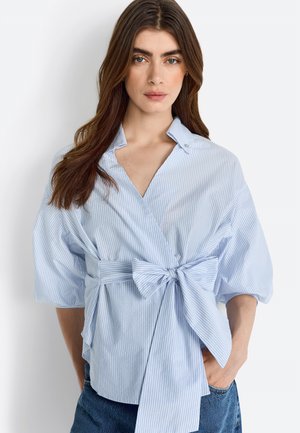 Helleblau gestreifte Bluse mit kurzen Ärmeln, einem Wickeldesign und einem vorderen Schleifenakzent. Hergestellt aus weichem Stoff mit glatter Textur.
