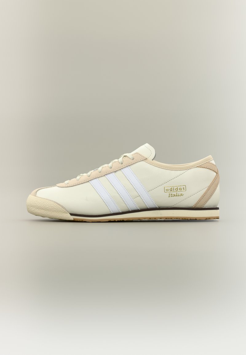 Κρεμ και μπεζ αθλητικό παπούτσι Adidas Italia με λευκές τριπλές ρίγες και μπεζ σόλα, εμφανισμένο σε προφίλ πλευράς σε ουδέτερο φόντο.