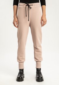 Ljusrosa joggingbyxor i mjukt tyg, med ribbat midjeband, dragsko-stängning och fållade ankeldesign. Matchas med svarta klumpiga stövlar.