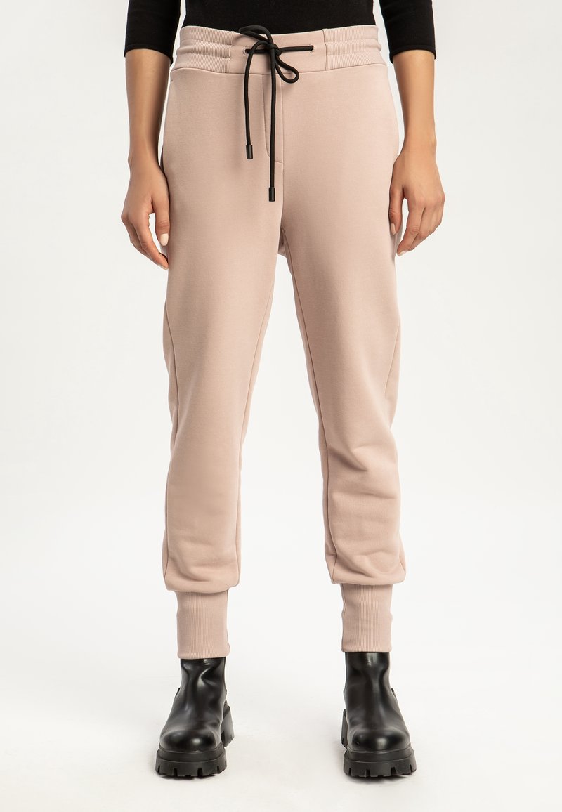 Ljusrosa joggingbyxor i mjukt tyg, med ribbat midjeband, dragsko-stängning och fållade ankeldesign. Matchas med svarta klumpiga stövlar.