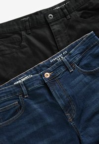 Două perechi de pantaloni straight-fit: o pereche din bumbac negru și una din denim albastru închis. Detalii notabile includ un sistem de închidere cu nasture și cusături în contrast.