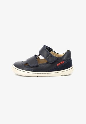 Zapato infantil de cuero azul marino con dos correas de Velcro, perforaciones para la transpirabilidad, suela blanca en contraste y acento de logo rojo.