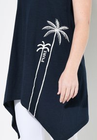 Túnica en azul marino con un dobladillo asimétrico, que presenta gráficos de palmeras blancas y el texto "PURE", confeccionada en una suave tela texturizada.
