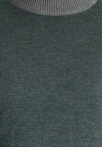 Primo piano di un maglione lavorato a maglia verde scuro con colletto alto a coste grigio, che mette in evidenza un tessuto testurizzato con un motivo sottile.