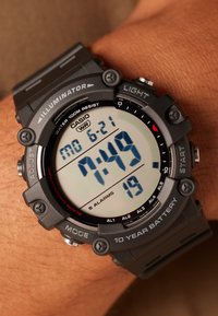 Montre numérique noire avec un grand affichage. Caractéristiques : étanchéité jusqu'à 100 mètres, cinq alarmes et une batterie d'une durée de dix ans. Bracelet en résine.